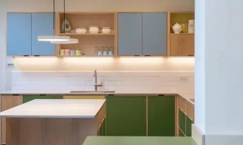 Modern kitchen with green and blue cabinets, open shelves, and a central island under a hanging light.