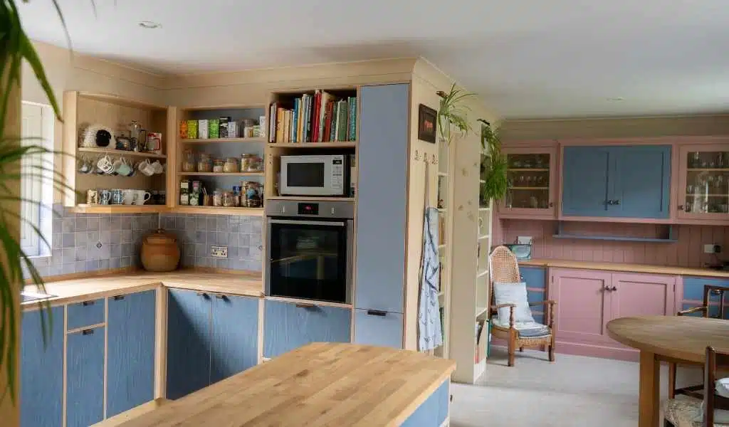 Cozy kitchen with colorful cabinets, open shelves, and a microwave. There's a dining area with wooden chairs.