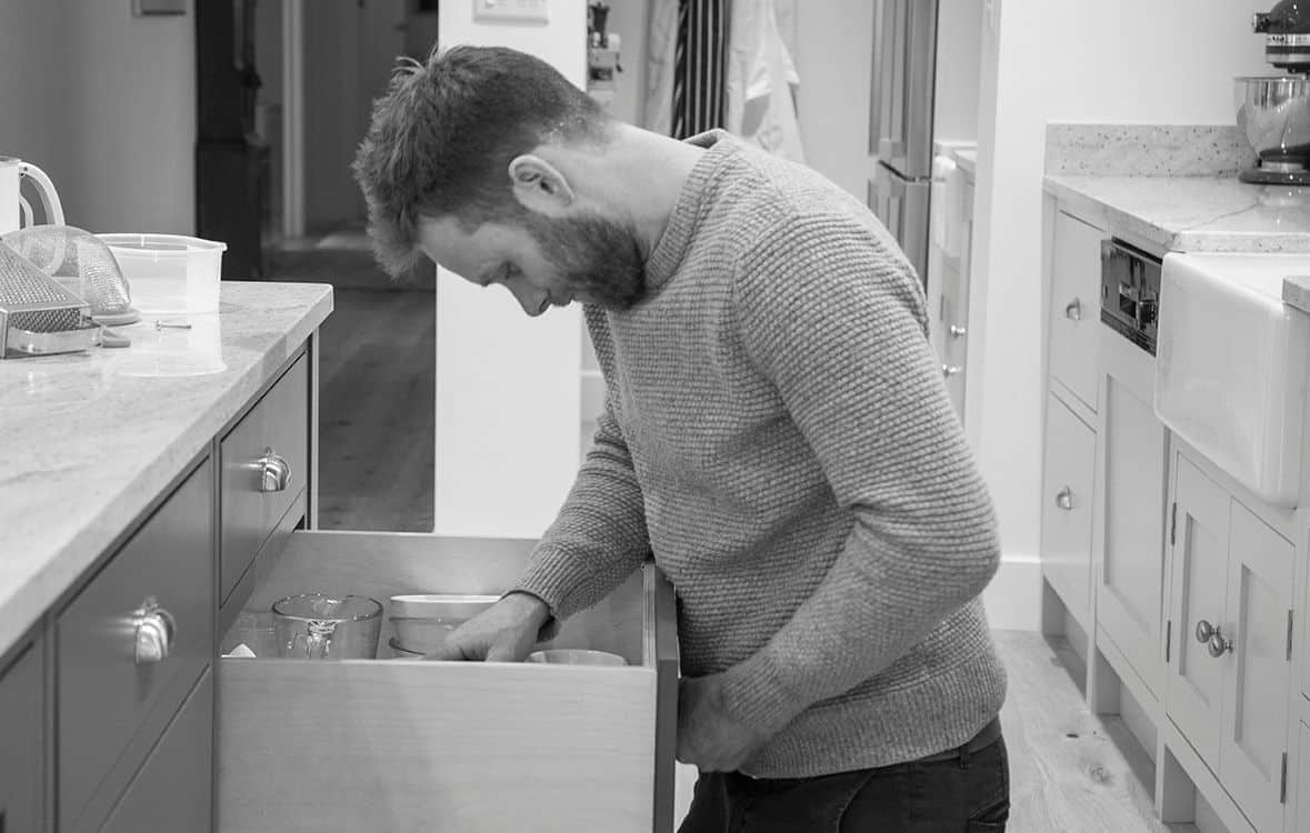 Man in a kitchen looking inside an open drawer with cups and bowls.