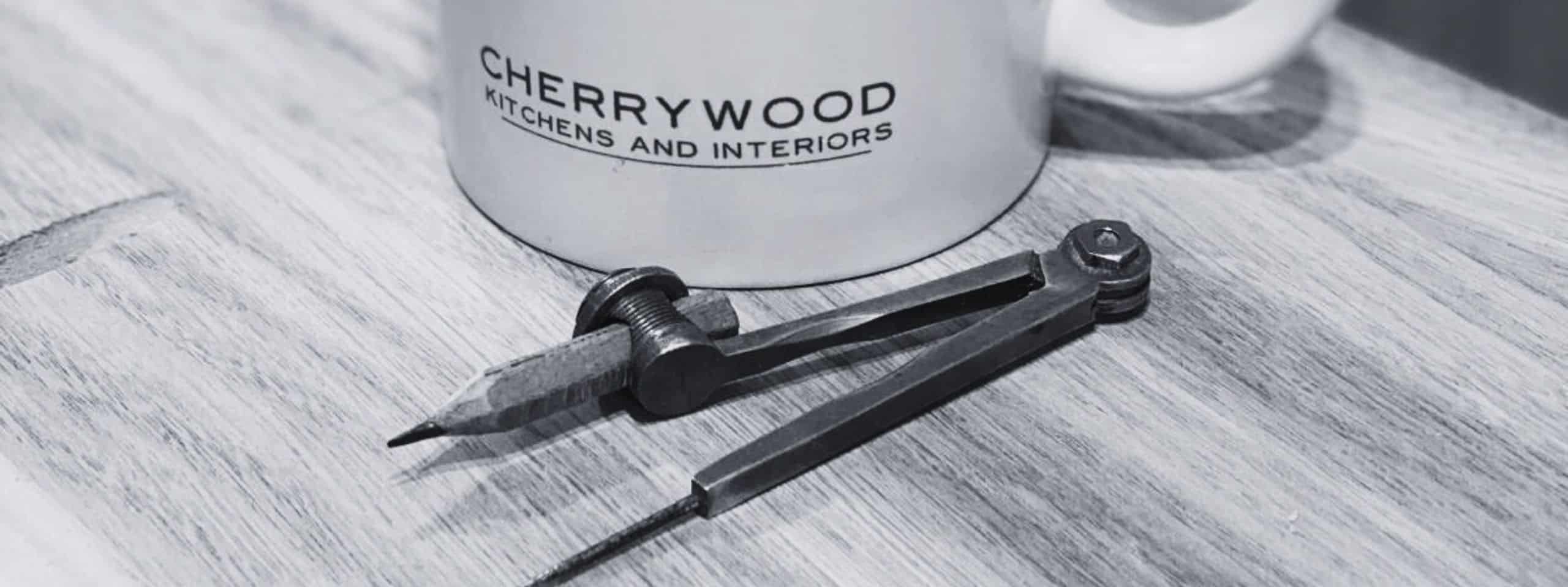 A mug with "Cherrywood Kitchens and Interiors" and an old compass pencil on a wooden table.