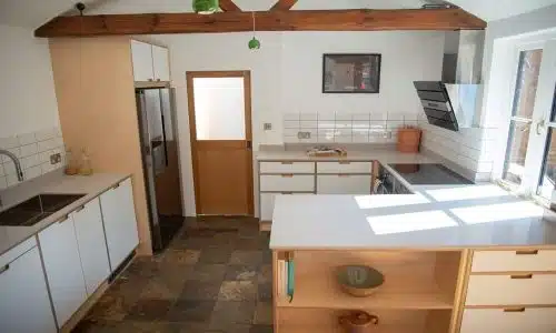 Spacious kitchen with white cabinets, wooden beams, and ample natural light.