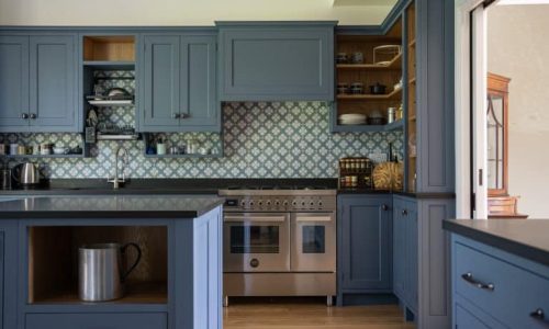 A modern kitchen with blue cabinets, patterned tiles, and stainless steel appliances.