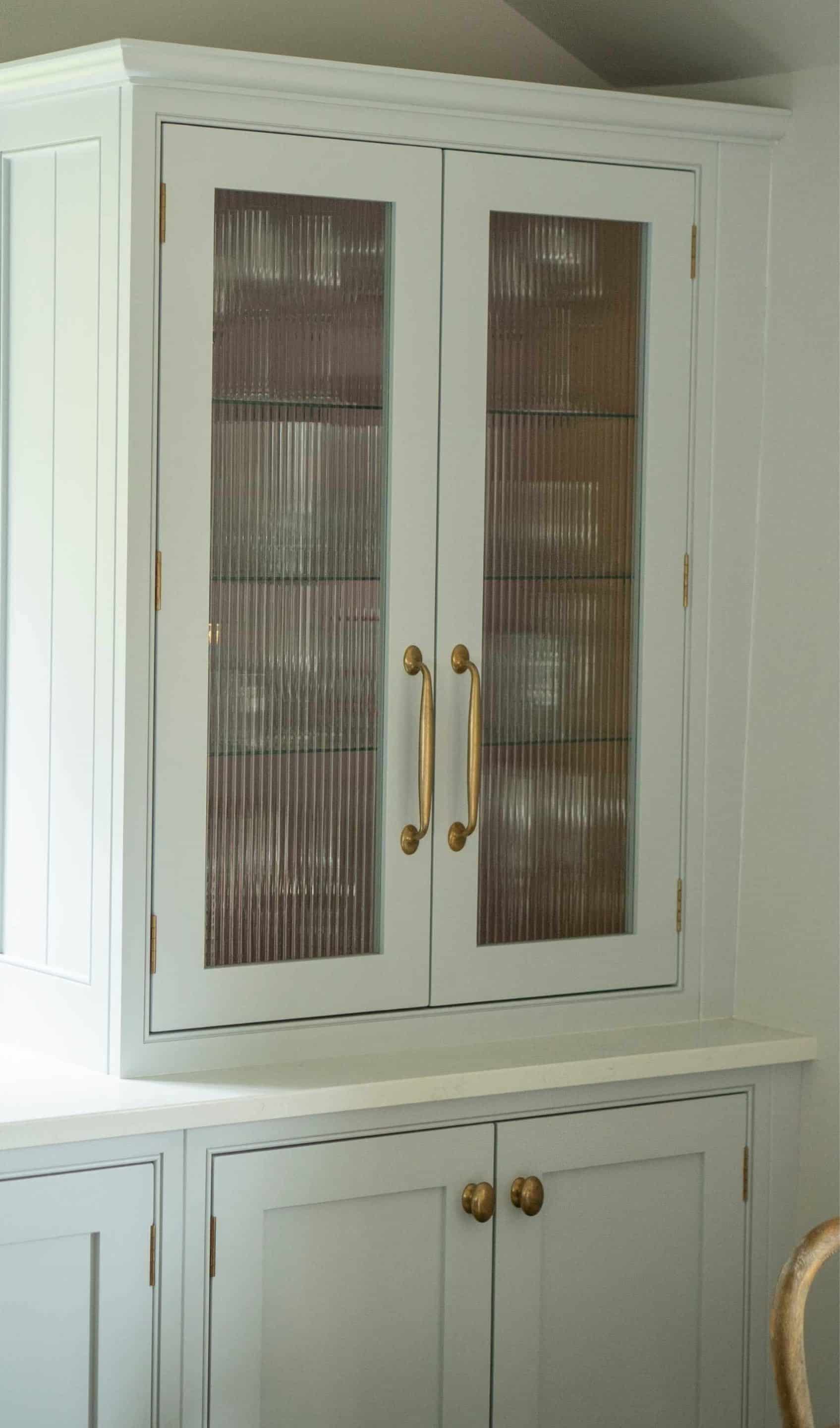 Light gray cabinet with ribbed glass doors and brass handles.