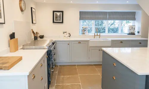 Modern kitchen with white cabinets, stone floor, and large window.