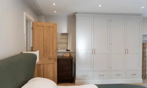 Bedroom with a green bed, wooden door, white wardrobe, and a small dresser.