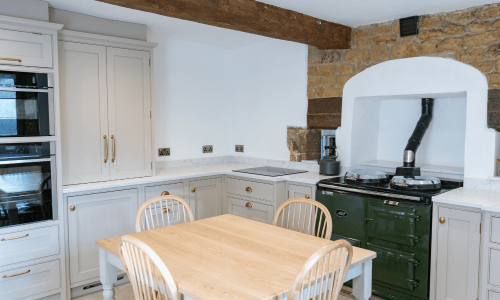 Rustic kitchen with wooden table, chairs, stone accent, and a traditional green stove.