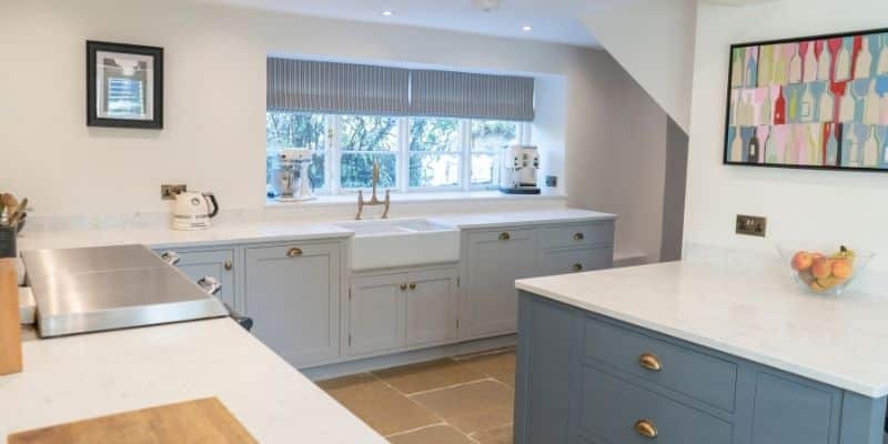 Modern kitchen with grey cabinets, white countertops, a farmhouse sink, and a window with blinds.