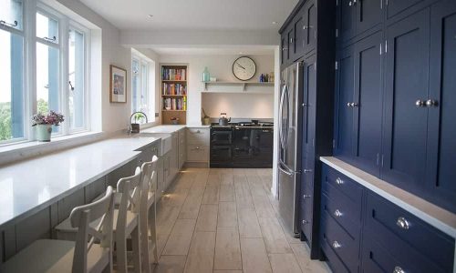Modern kitchen with blue cabinets, white countertops, wooden floor, and a large window.
