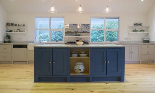 Modern kitchen with a blue island, light wood floors, and large windows.