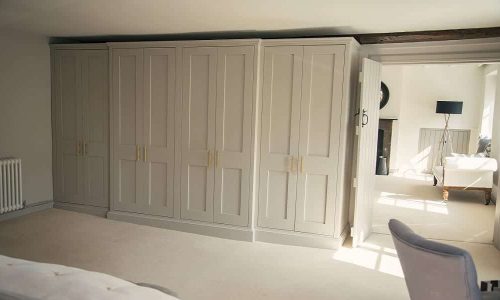 A spacious bedroom with fitted wardrobes and a glimpse of an adjoining room with a chair and some decor.