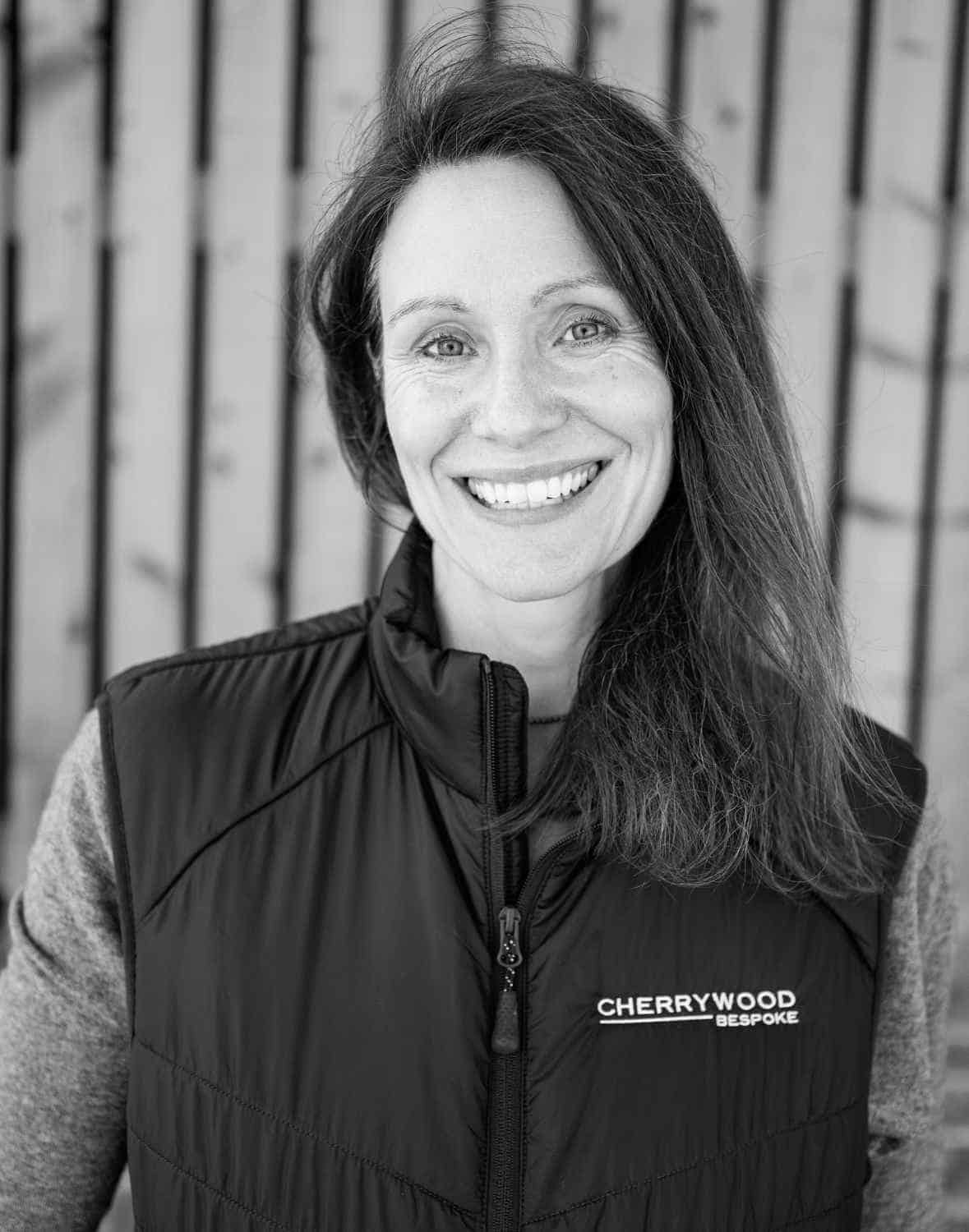Smiling person wearing a Cherrywood-branded vest, standing in front of a wooden backdrop.