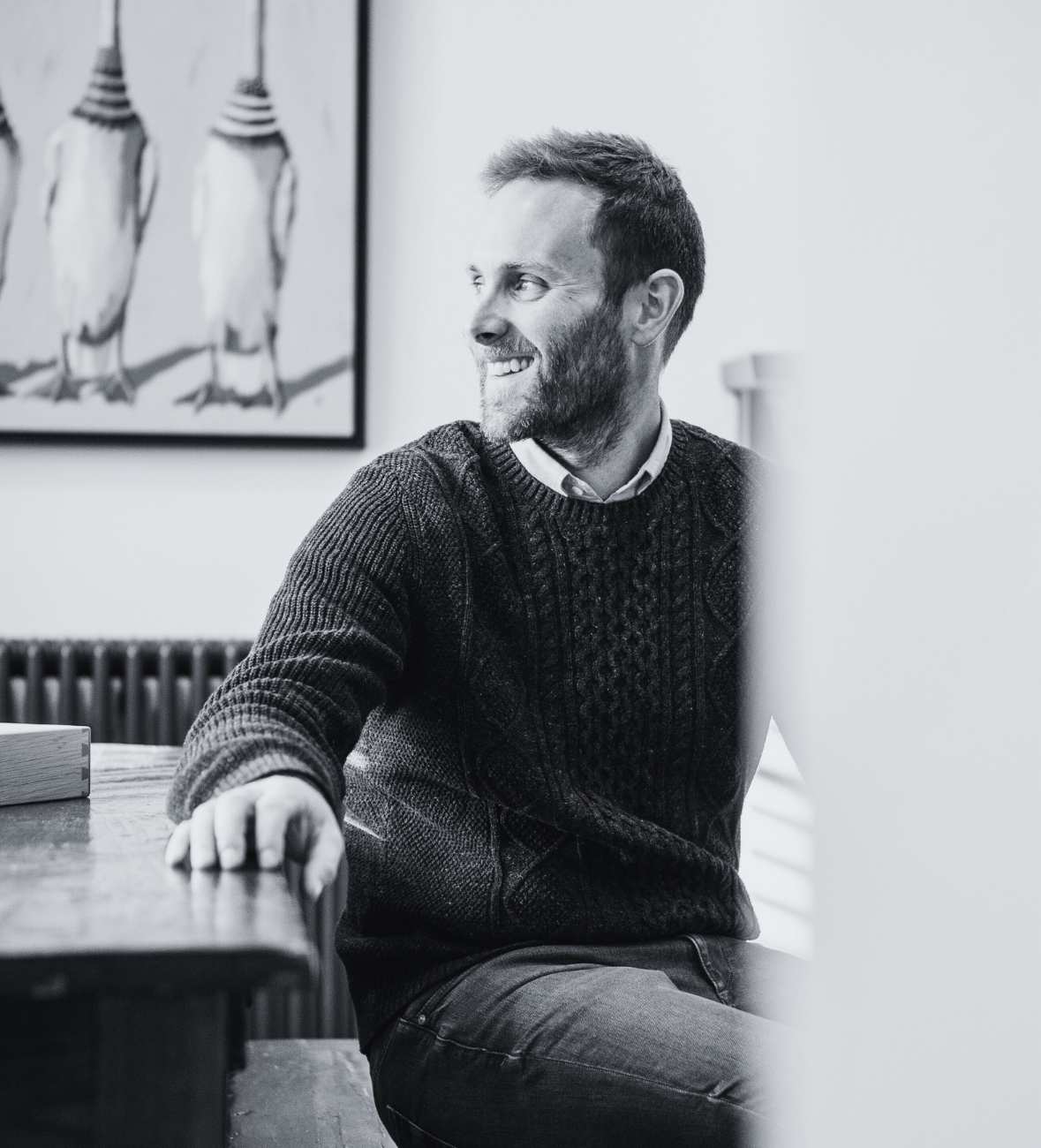 Man sitting at a table, looking sideways, with penguin art in the background.