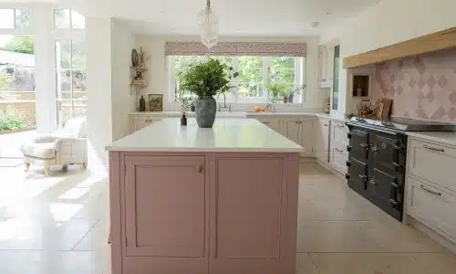 Bright kitchen with a pink island, white countertops, and large windows letting in natural light.