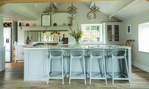 Bright modern kitchen with a large island, bar stools, wood floors, and decorative lighting.