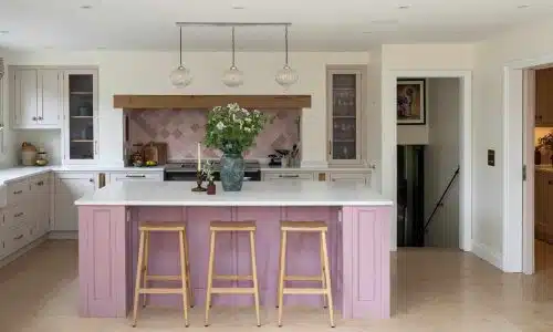 Modern kitchen with a pink island, wooden stools, and white cabinets.
