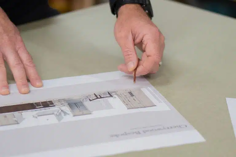 Kitchen with white chairs, wooden floor, books on shelves, and a clock above the stove.