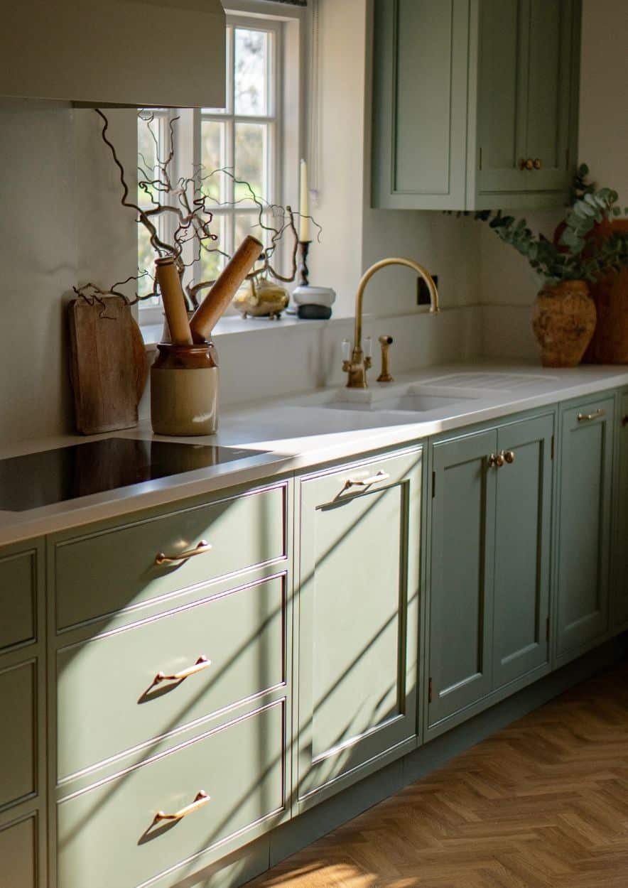 18 Bright kitchen with wooden floors, white cabinets, and a window above the sink.