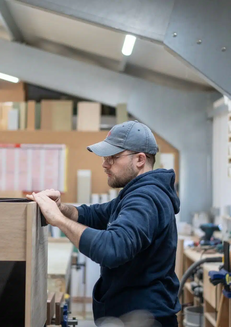 Person wearing gloves, adjusting a metal piece against a blue guide on a workbench.