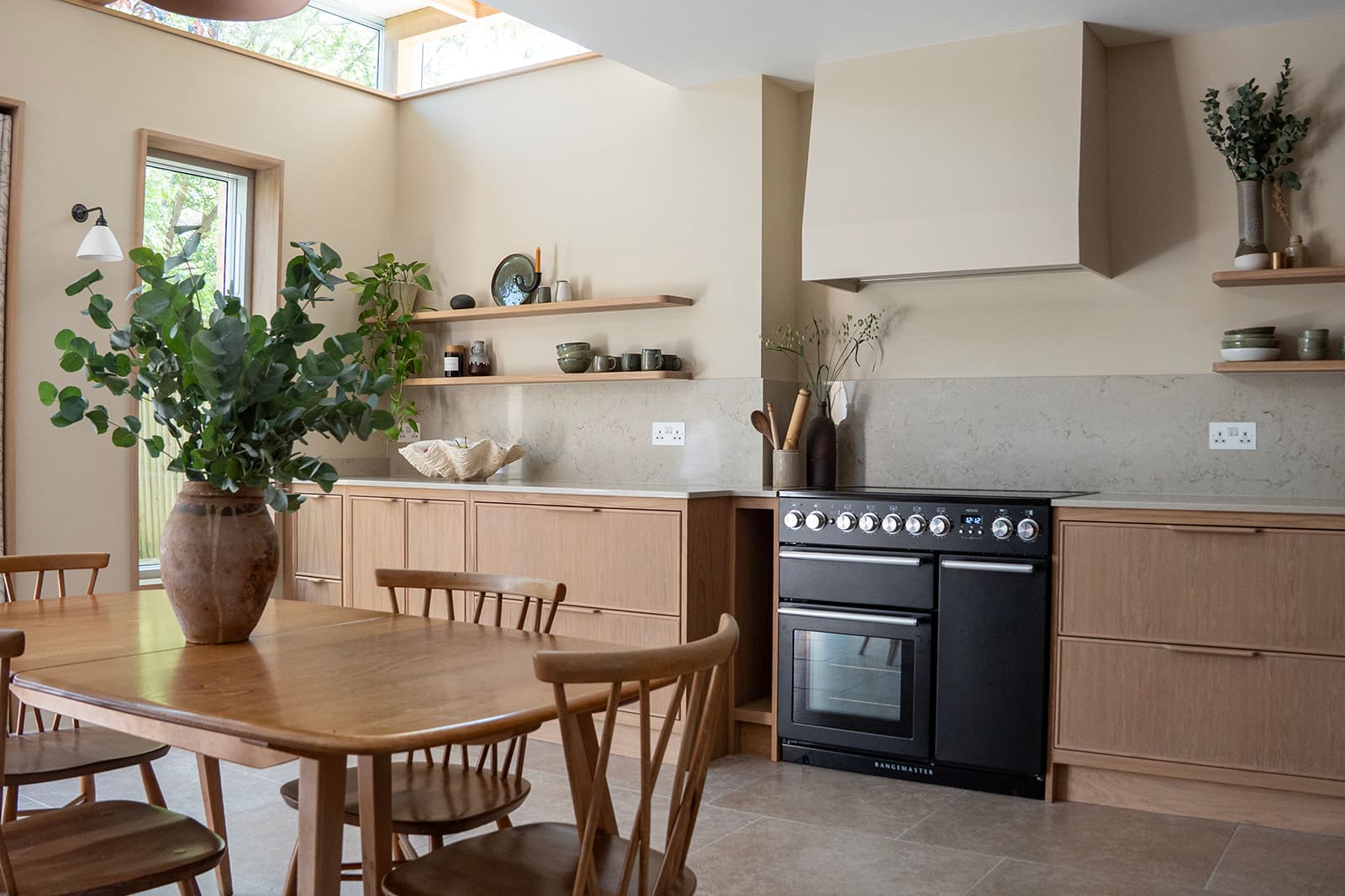 Bright kitchen with white cabinets, wooden stools, open shelves, and sunlight streaming through the windows.